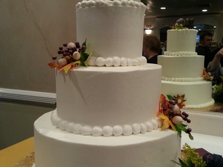 3 tier round white wedding cake, accented fall themed foliage, topped with 2 owls dressed as bride and groom.
